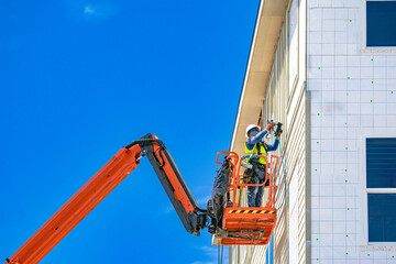 Construction worker installing vertical siding with pneumatic nail gun from cherry picker boom lift in USA © Andrei Liashchou