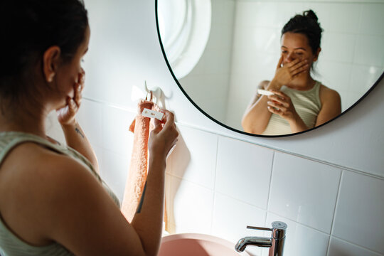 Woman reacting to pregnancy test in bathroom mirror