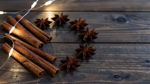 Warm cinnamon sticks and star anise glow softly on rustic wooden surface.