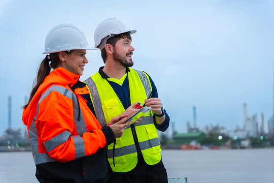 Industrial engineers team with tablet and walkie talkie outdoors in rainy weather at shipping port, logistic managers in safety gear discussing project details during rain at industrial cargo yard