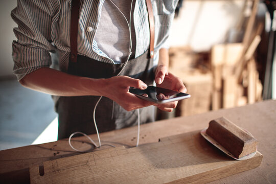 Artisan using smartphone at woodworking workshop bench