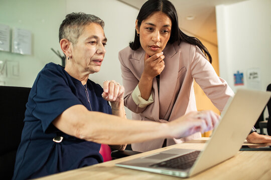 Two businesswomen collaborating on laptop in modern office