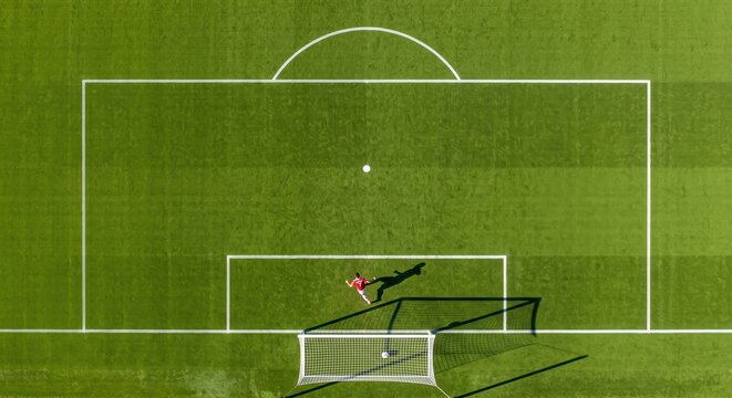 Aerial top down view of a single football player in a red kit scoring a goal on a minimalist green pitch