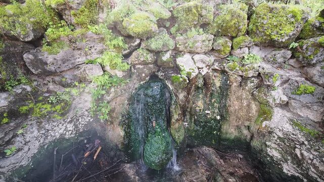 Water flowing from moss covered stone wall.