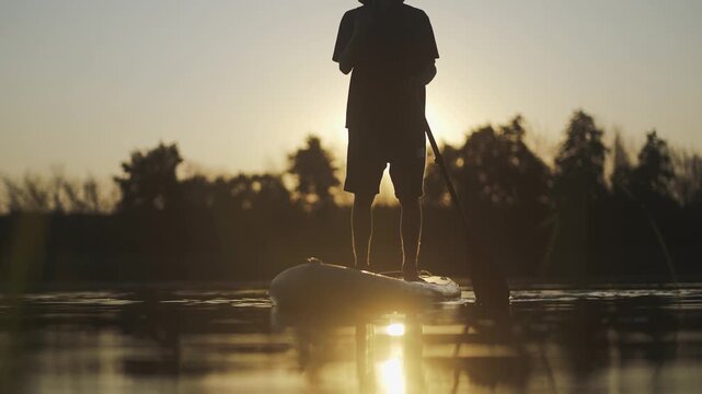 Sup board boad man. A man stands on a paddleboard as the sun sets, reflecting on the water. The man enjoys peaceful moments on the calm water during sunset.