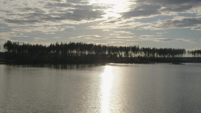 Sun glare over calm lake with forest silhouette on horizon