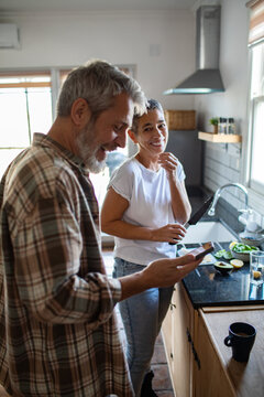 Happy mature couple cooking and using smartphone in home kitchen