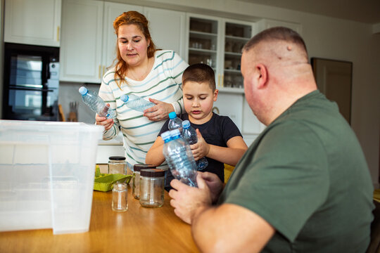 Family sorting plastic bottles and glass jars for recycling in a home kitchen