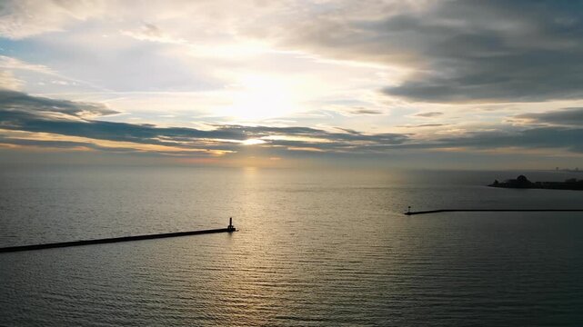 Aerial View of Sunset Over Calm Sea with Lighthouse and Breakwaters at Golden Hour