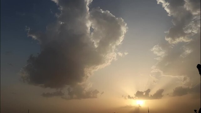 Time-lapse of dramatic sunset with sun rays piercing through cumulus clouds in golden hour