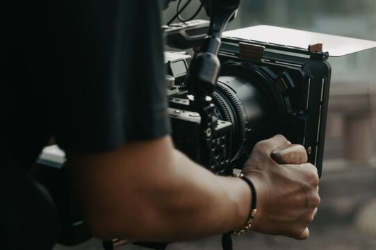 Hands grip camera steady during filming session. Focus and precision evident in operator's posture. Soft bokeh hints at professional film or photography setup