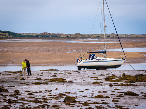 Couple Walking by Sailboat at Low Tide on Ravenglass Estuary in Cumbria