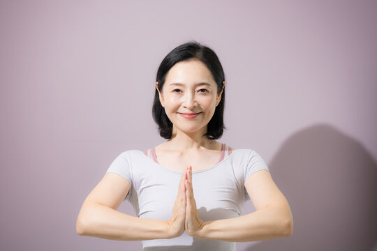 胸の前で手を合わせてヨガのポーズをする女性、心身を整えてリラックスする日本人ミドル女性カメラ目線