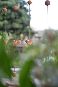 hanging handcrafted terracotta bird mobiles on strings with blurred garden foliage, rustic luxury brazilian event decoration, selective focus vertical shot