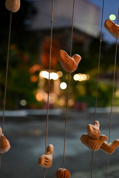 clay bird figures hanging on vertical strings at dusk, artisan installation outdoor night background, decorative ceramic craft concept   