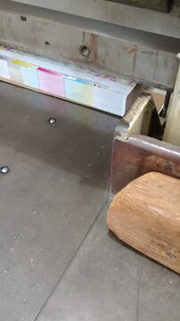 Printing press operator cutting wedding stationery paper stack using a heavy industrial guillotine machine in a professional print shop production facility.