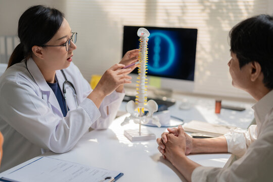 Asian Female Orthopedic Doctor Demonstrating Spinal Model to Patient in Office