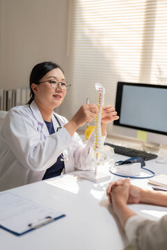 Asian Female Orthopedic Doctor Demonstrating Spinal Model to Patient in Office