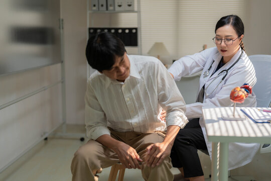 Asian Female Doctor Examining Senior Patient Suffering from Severe Lower Back Pain