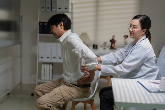 Asian Female Doctor Examining Senior Patient Suffering from Severe Lower Back Pain