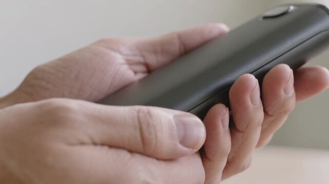 A close-up shot of two hands rotating and adjusting the grip on a matte black smartphone, focusing on the phone's rear camera edge and the fingers repositioning around it.