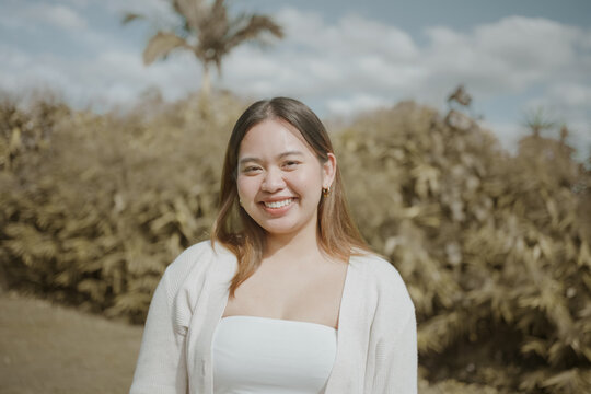 Asian woman, smiling, portrait, happy, outdoor, young adult, ethnicity enjoying a sunny day in a lush green garden setting with a cheerful and confident expression on her face.