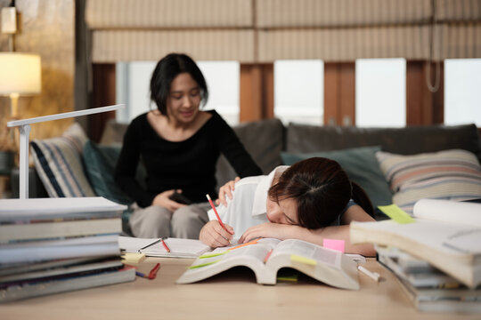 Two College Asian friends, teenage girl tired and burned out from overwhelmed homeschooling, study pile of books, stressed learning at home, her friend wakes up while napping, education exam support.