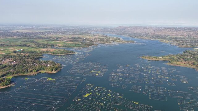 Aerial view of vast fish farming ponds. Rows of nets stretch across calm blue waters at Waduk Karangkates