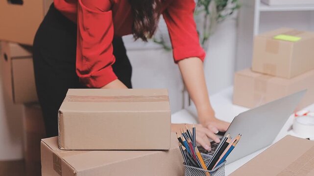 Close up with Start up small business, SME female owner using laptop checking order online to prepare to pack a box of goods for sale to customers, sme business idea.