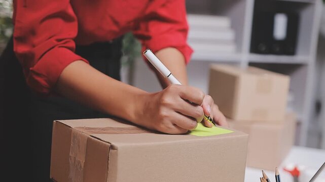 Close up with Start up small business, SME female owner using laptop checking order online to prepare to pack a box of goods for sale to customers, sme business idea.