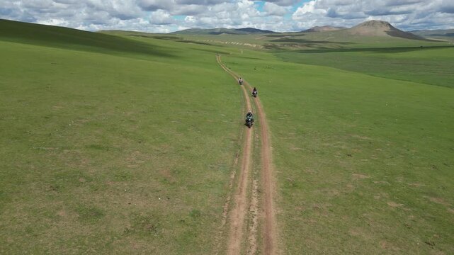 Motorcyclists ride remote grass road on vast green Mongolian steppe