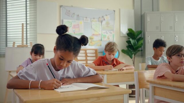 Diverse boy and girl students taking notes in notebooks in classroom. 