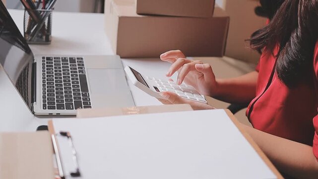 Close up with Start up small business, SME female owner using laptop checking order online to prepare to pack a box of goods for sale to customers, sme business idea.