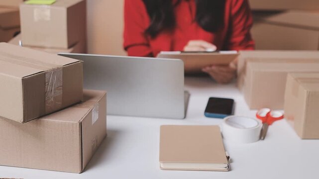 Close up with Start up small business, SME female owner using laptop checking order online to prepare to pack a box of goods for sale to customers, sme business idea.
