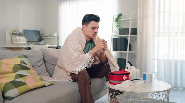 Latino sick man feeling cold while sitting on sofa in living room at home. 