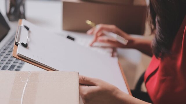 Close up with Start up small business, SME female owner using laptop checking order online to prepare to pack a box of goods for sale to customers, sme business idea.
