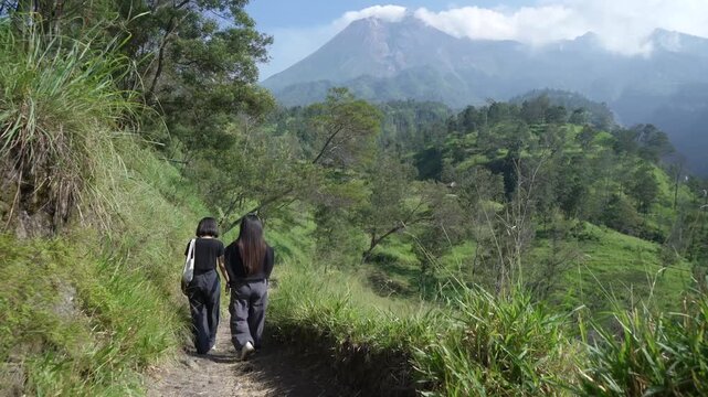 Two Gen Z Women Hiking on a Mountain Trail with Mount Merapi in Indonesia