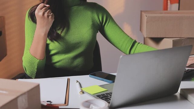 Close up with Start up small business, SME female owner using laptop checking order online to prepare to pack a box of goods for sale to customers, sme business idea.