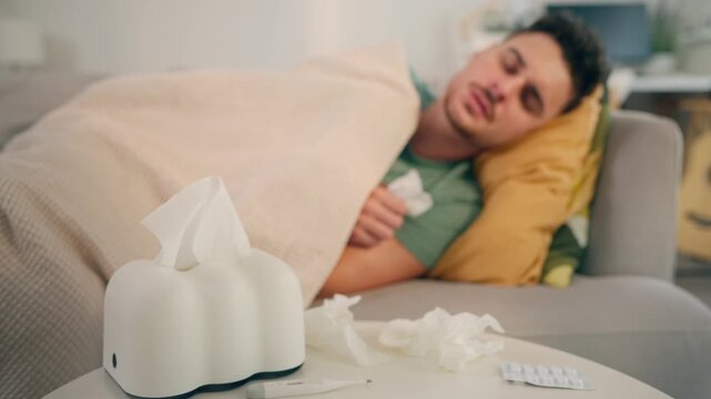 Latino sick man feeling cold while lying on sofa in living room at home. 
