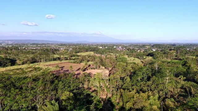Green hills roll under bright blue skies. Distant mountains fade into hazy at rural Malang
