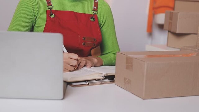 Close up with Start up small business, SME female owner using laptop checking order online to prepare to pack a box of goods for sale to customers, sme business idea.