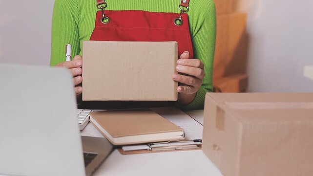 Close up with Start up small business, SME female owner using laptop checking order online to prepare to pack a box of goods for sale to customers, sme business idea.
