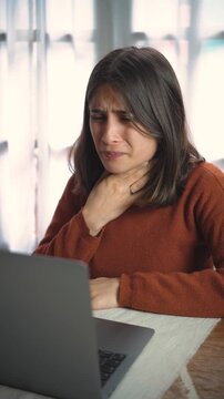 Young Hispanic woman on a work video call begins coughing heavily and experiencing throat pain, portraying illness, workplace discomfort, and the challenge of working while sick.
