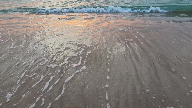 Wide angle shot of gentle sea waves rolling onto a sandy beach.
