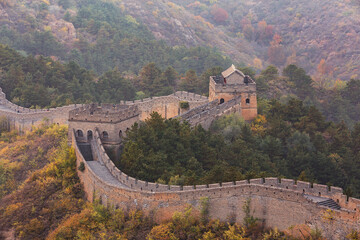 Fototapeta premium Ancient stone fortification winds across autumn mountain slopes, flanked by dense forests with seasonal foliage.