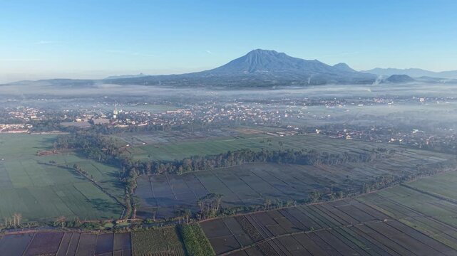 Morning mist blankets Kepanjen rice paddies with distant Mountain Kawi backdrop and scattered village settlement.