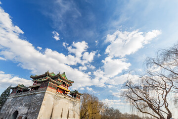 An ancient traditional Chinese pavilion stands under a bright blue sky with white clouds, surrounded by bare willow trees.  © tai