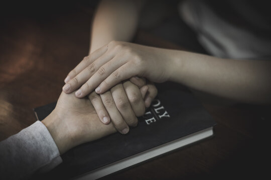 Group Prayer and Christian Fellowship with Hands Joined in Faith beside a Holy Bible and Cross.