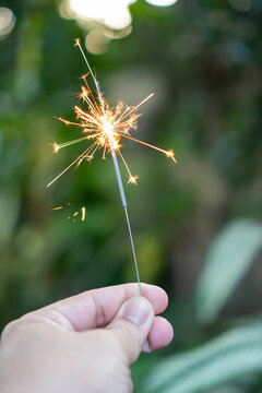 Hand holding glowing sparkler firework with bright flame, light, and spark outdoors, bringing pure joy, excitement, and happiness to holiday celebration event