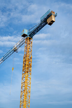 Tall yellow metal construction tower crane reaches toward bright blue sky, showcasing powerful machinery and industry progress in ambitious building projects